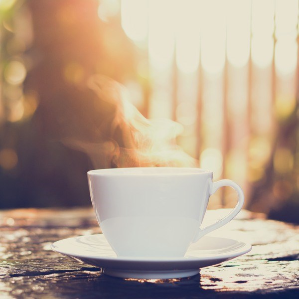 Hot coffee on old wood table with blur background of sunlight shining through the trees - soft focus, vintage tone